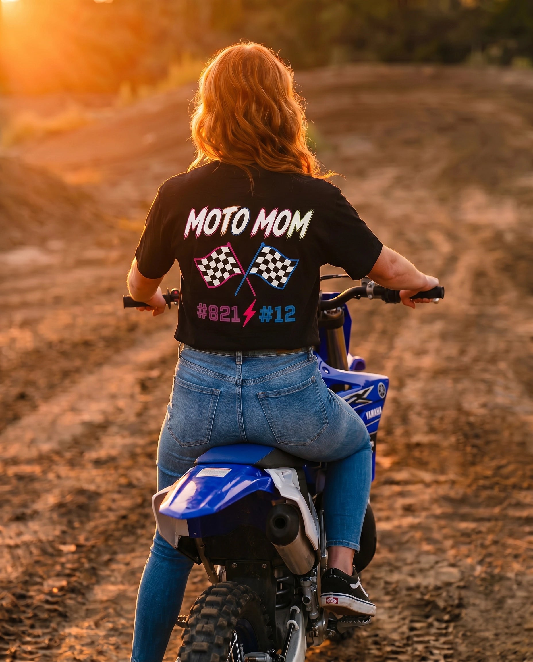 Moto Mom shirt back graphic - woman sitting on blue Yamaha dirt bike on motocross track at golden hour